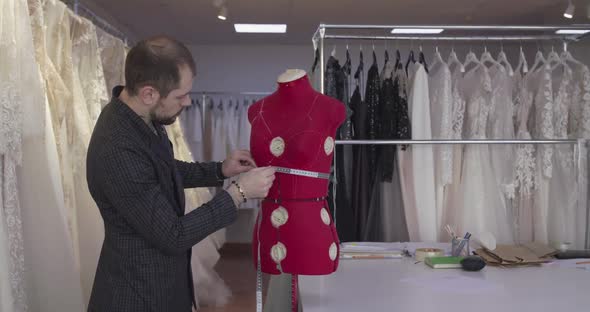 Handsome Designer Measures Waist on Female Sliding Tailor Dummy in Atelier alt