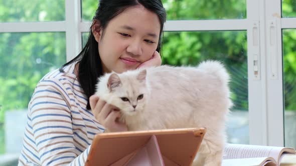 Happy Asian Girl Playing With Pet Cat While Doing Homework alt