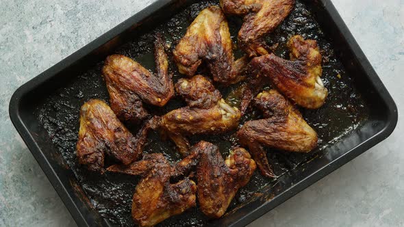 Grilled Chicken Wings in Spices in Black Metal Baking Tray on Stone Table
