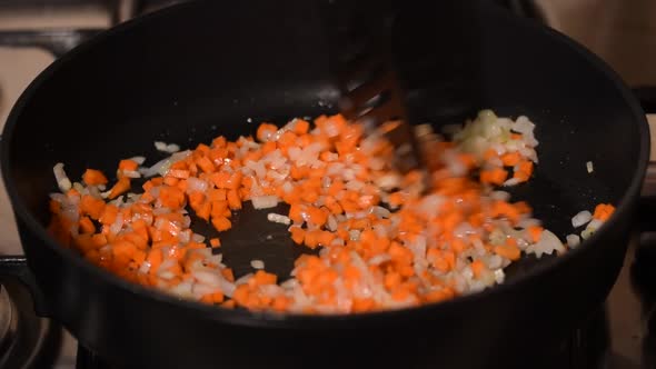 Female hands stirring the frying onions and carrots in frying pan.	 alt