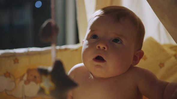 A Laughing Baby Playing with Toys of Hanging Mobile and Looking at Camera alt