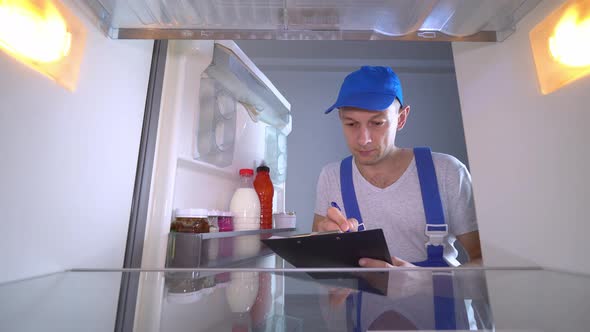 The refrigerator repairman opens the door and the list of works