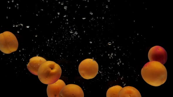 Slow Motion Apricots Falling Into Transparent Water on Black Background alt