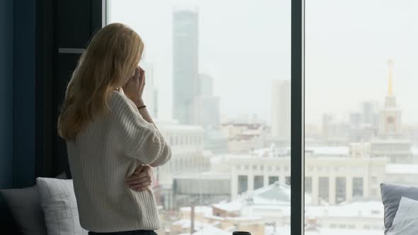 caucasian woman talking on the phone by a large window overlooking the city