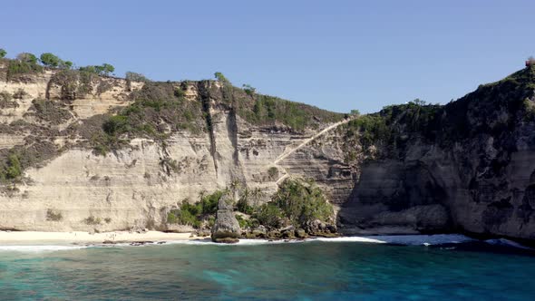 Sandy Diamond Beach in Nusa Penida island Indonesia with rock walls behind, Aerial dolly out reveal alt