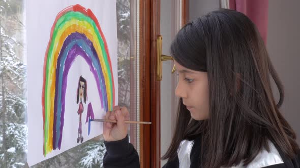 The girl is drawing a rainbow on the glass. alt