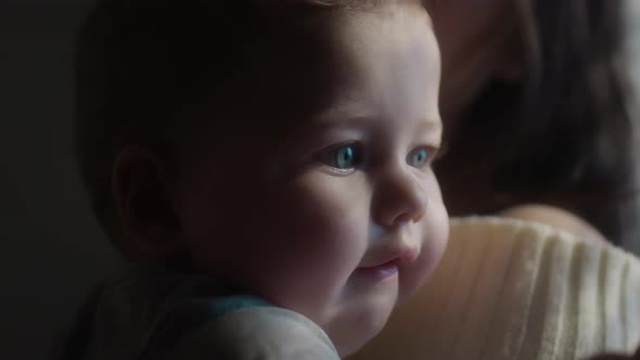 The Baby is in the Arms of His Mother Looks with Blue Eyes alt