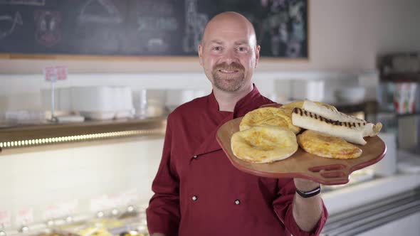 Bearded Male Caucasian Cook Posing with Tray with Cooked Tasty Pinza Indoors alt