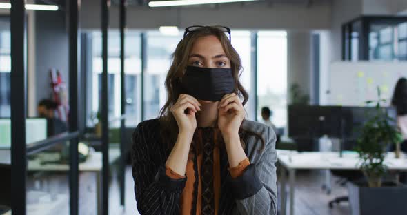 Portrait of caucasian businesswoman adjusting face mask standing in office and looking to camera alt