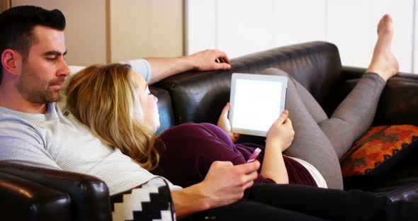 Couple using mobile phone and digital tablet on sofa alt