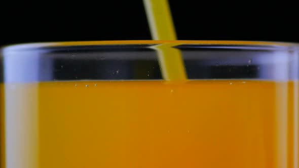 Close Up of Drinking Orange Soda with a Straw at Black Background