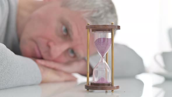 Upset Senior Old Man Looking at Hourglass in Anticipation at Home  alt