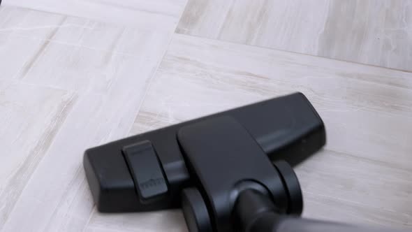A Vacuum Cleaner Brush Removes Trash From the Floor on the Tiles in the Room alt