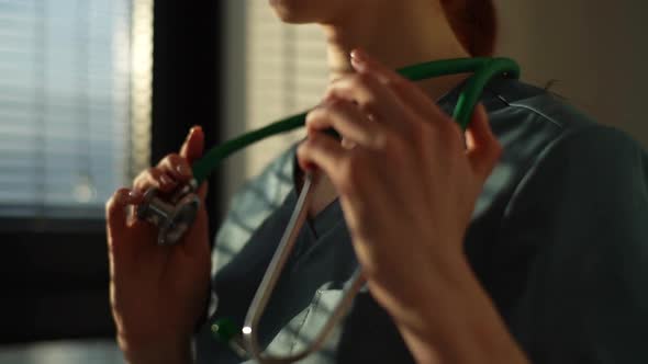 Closeup of Unrecognizable Female Doctor in Blue Green Uniform Putting on Stethoscope on Neck alt