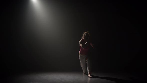 Female Practicing Capoeira in Darkness Under Spotlight in Studio alt