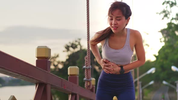 Asian young fit sport woman running and jogging in the park feeling pain on stomach during workout. alt