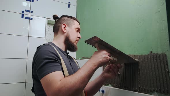 Repairman Applying Tile Adhesive with a Notched Trowel on the Bathroom Wall alt