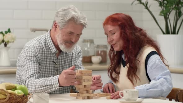 A Senior Couple in Their 60s and 70s Play a Board Game at Home Removing Wooden Cubes From a Tower