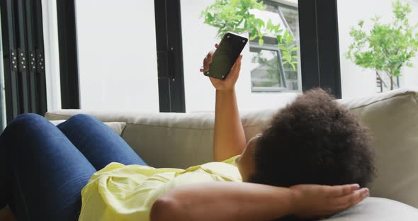 Video of plus size african american woman relaxing on sofa with smartphone alt