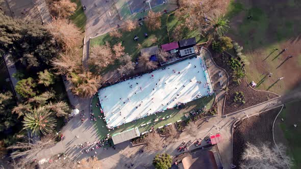 Overhead spiral boom up view of an ice skating rink with people, Parque Araucano, Santiago, Chile. alt