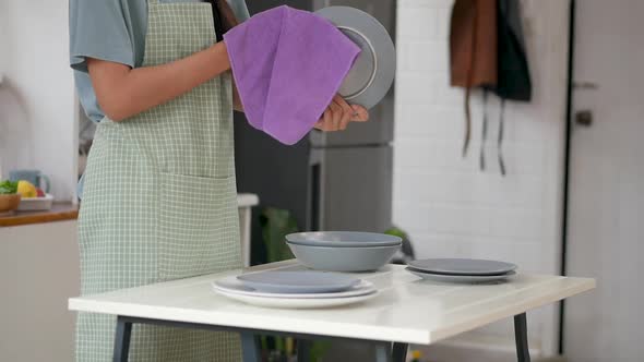 Young asian woman wiping dishware with a cotton towel in the kitchen at home.