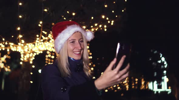 young beautiful blonde in Santa Claus hat, talking on video link in her phone alt