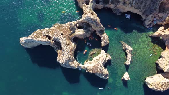 Drone shot of kayaks and boats passing in the ocean, people exploring caves and tunnels.