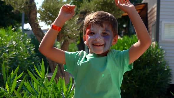 Cheerful Boy is Jumping Outdoors with Makeup in the Colors of a French Flag alt