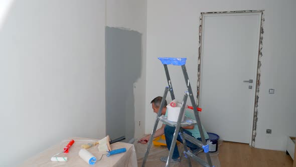 A Man in a Shirt Paints the Walls with a Roller Gray alt