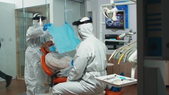 Nurse in Coverall Putting Dental Bib to Woman During Examining alt