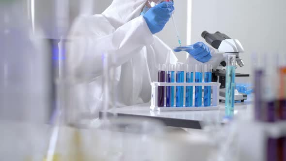 Scientist in PPE suite doing some research checking a liquid in a test tube at laboratory. alt