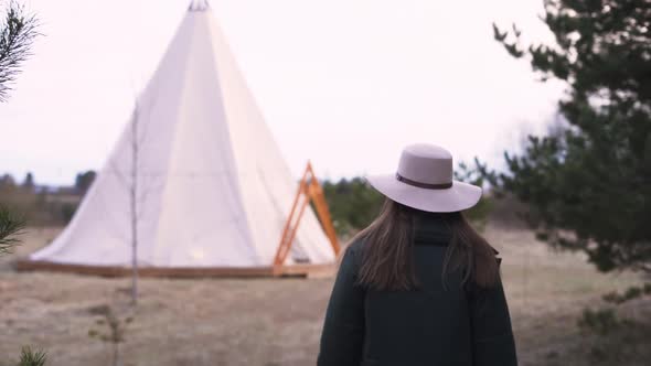 Young Beautiful Woman Walking Through Field Towards Teepee On Spring Winter Autumn Glamping Vacation