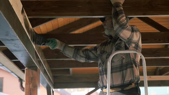 Painter Applies Paint with a Brush to a Wooden Structure alt
