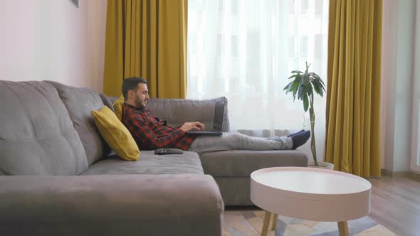 Man in Classic Square Shirt Lying on a Couch and Video Conference on Laptop PC at Home alt