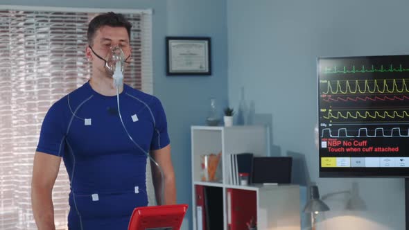 Fit Athlete in Oxygen Mask Walking on Treadmill with Electrodees Connected on Him alt
