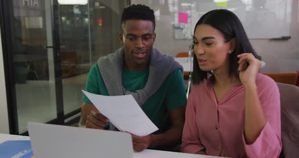 Diverse male and female business colleagues sitting at desk analyzing document and smiling alt