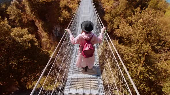 Woman Walks on Footbridge Over Gorge Among Yellowed Trees alt