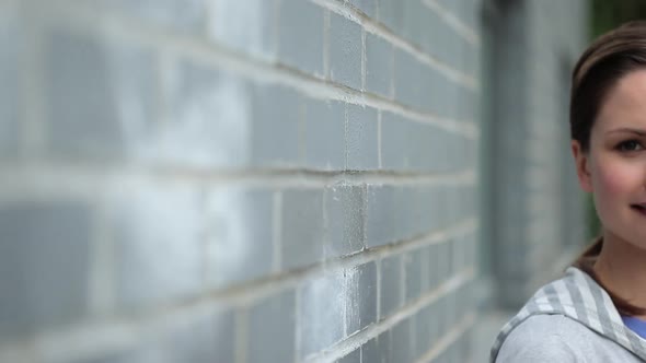 Young woman leaning on wall and smiling at camera alt