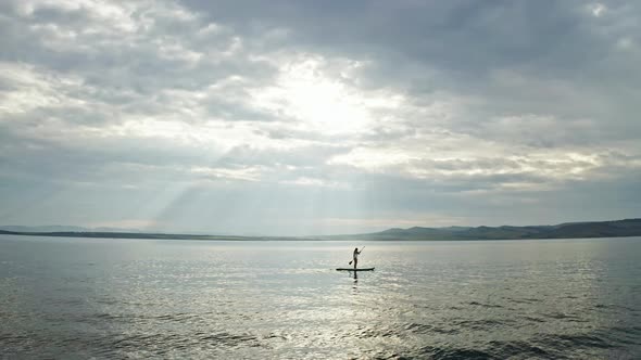Drone Shot of a Silhouette of a Young Woman Floating on a Board with a Paddle alt