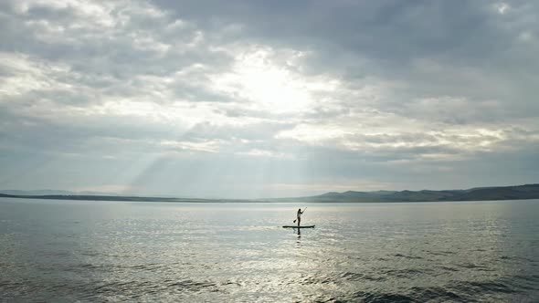 Drone Shot of a Silhouette of a Young Woman Floating on a Board with a Paddle