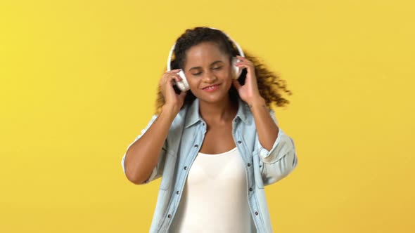 African American woman touching headphones while listening to music and dancing