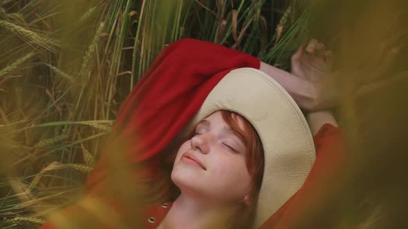 Close Up of Romantic Redhead Girl Resting Lying in Wheat Field with Pleased Relaxed Smile