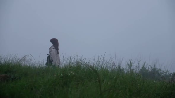 Slow motion of a female traveler walking through the greenery mountains on foggy day