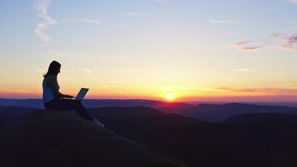 A Freelance Woman Working at the Top of a Mountain at Sunset Tiredly Stretches Her Hands Up and