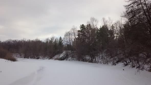 Low Flight of Drone Over Frozen Riverbed in Forest