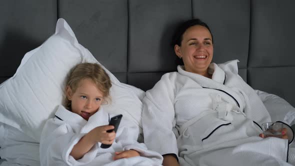 Young Woman with Daughter in Bathrobes Watch TV alt