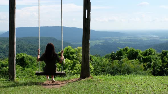 Rear view of a woman sitting on a swing looking at a beautiful mountains and green nature background