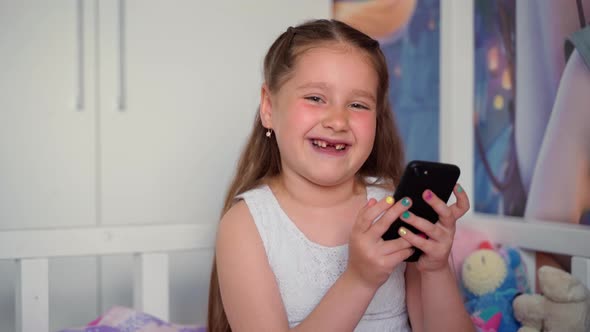 Girl holding smartphone looking at camera smiling. Portrait of cute cheerful young child person alt