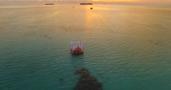 Aerial drone view of a man and woman having dinner on a floating raft boat at sunset alt