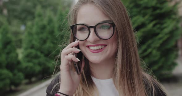 Portrait of Happy Young Girl in Glasses Speaking on a Phone with Smile on Face alt